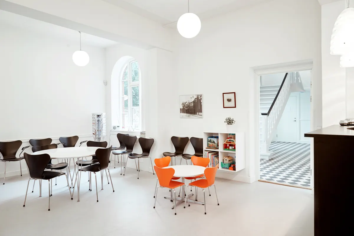Venteområde med orange stole og legetøjshylde.