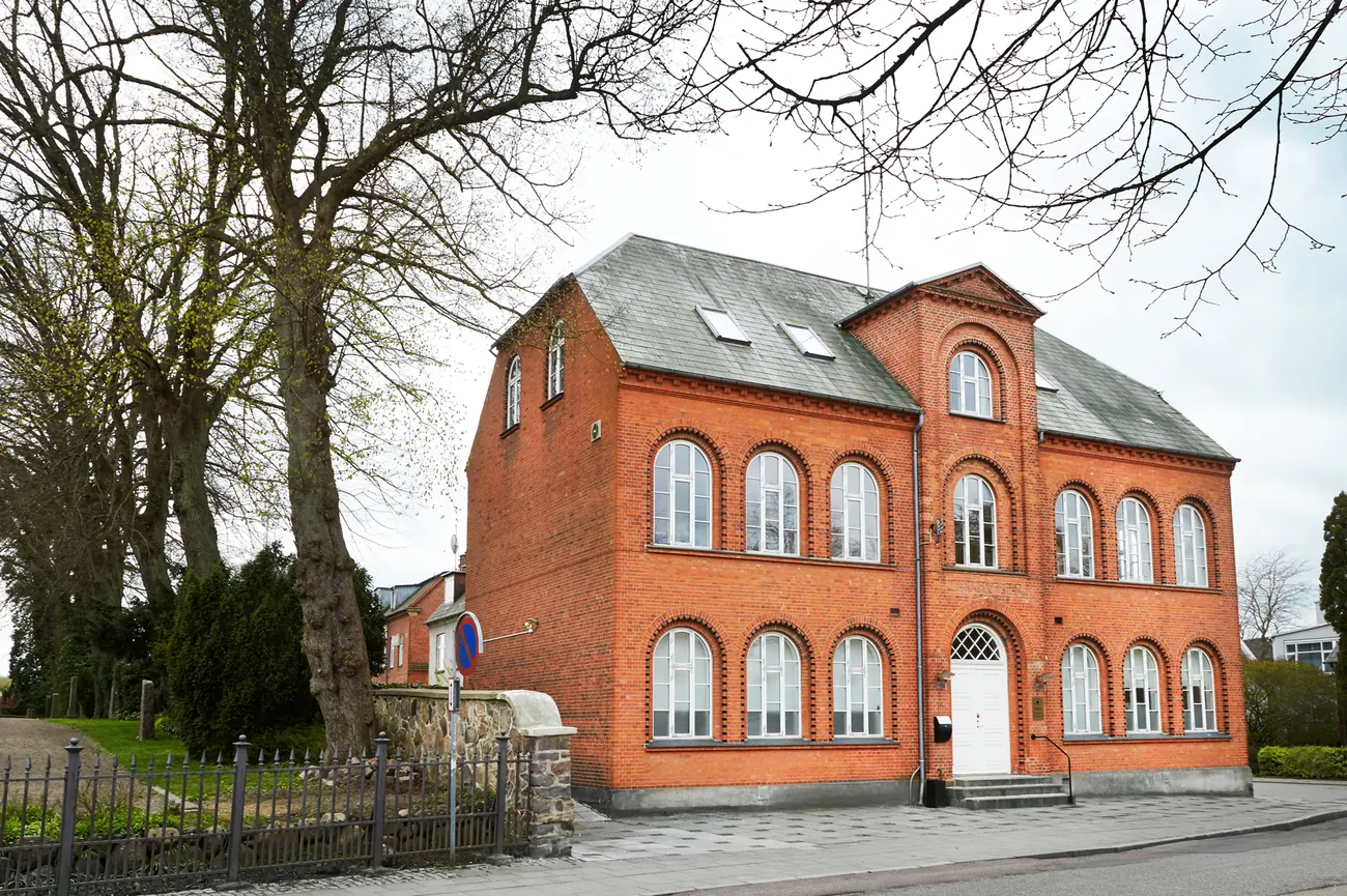 Foreningshuset set fra gaden — rød murstensbygning med rundbuede vinduer og store træer foran.